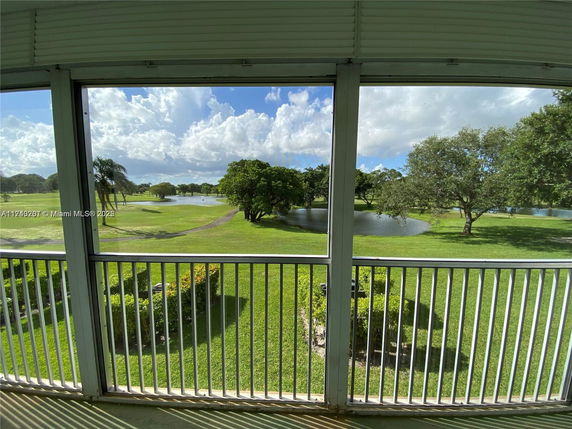 Panoramic view of grassy landscape with trees and a small pond, seen through a railing.