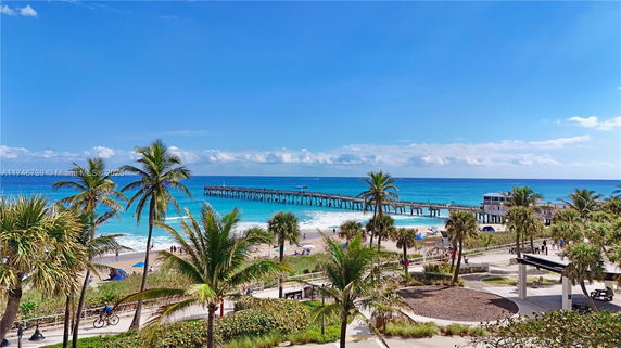 View of a beach with palm trees and a pier extending into the ocean.