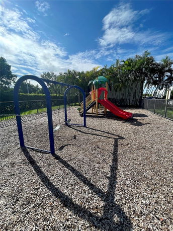 Outdoor playground with swings and a slide surrounded by trees and fencing.