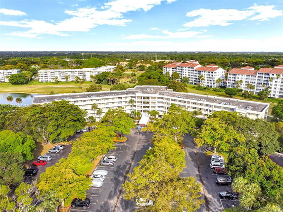 Aerial view of apartment buildings surrounded by trees and parking area.