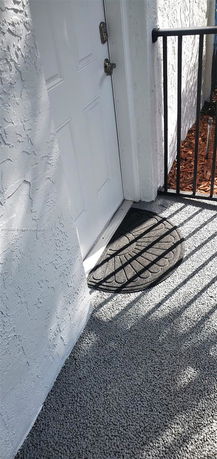 Exterior view of a white door with a welcome mat on a textured surface.