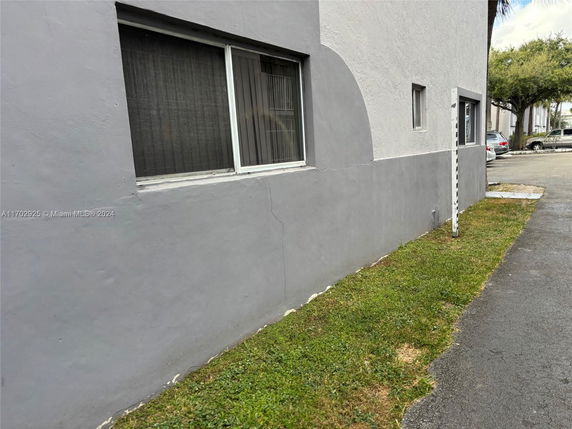 Side view of a building with gray exterior walls and windows, adjacent to a parking area.
