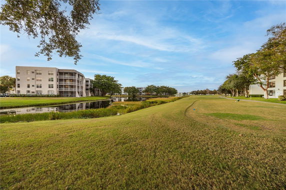 View of a residential building near a water body with trees and grass.