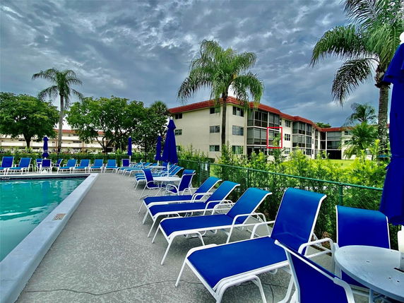 Outdoor swimming pool area with lounge chairs and view of a multi-story building in the background.