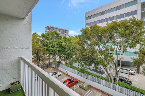 View from a balcony showing a parking area and buildings with trees.