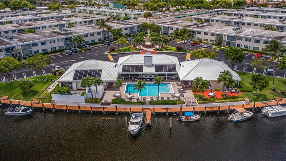 Aerial view of a building with a swimming pool and docks, surrounded by multiple structures and parking areas.