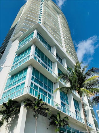 Front view of a modern multi-story building with glass balconies and palm trees.