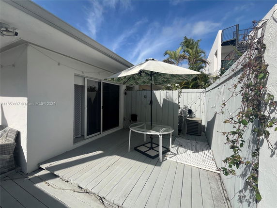 Patio area with a table and umbrella next to a white house with sliding glass doors.