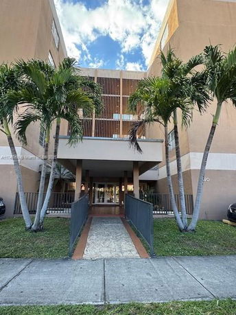 Front view of a multi-story apartment building with palm trees and an entrance walkway.