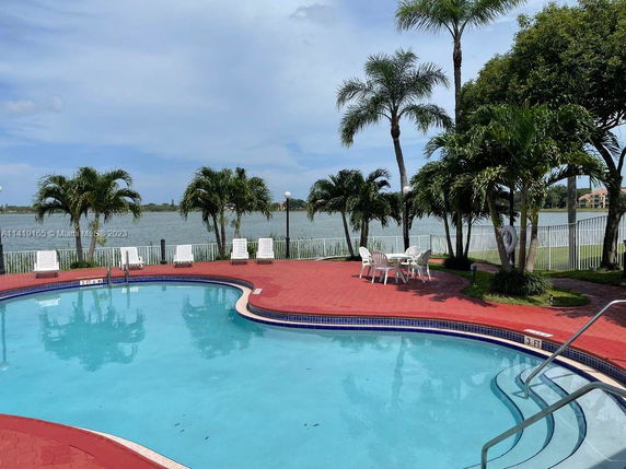 Outdoor swimming pool area with surrounding palm trees and a view of a lake.