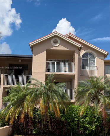 Front view of a two-story building with balconies and palm trees.