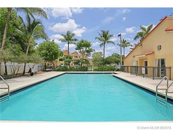 Outdoor swimming pool with palm trees and buildings in the background.