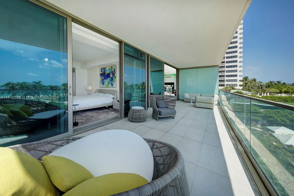 Balcony view from a modern apartment with glass railing, overlooking a distant high-rise and greenery.