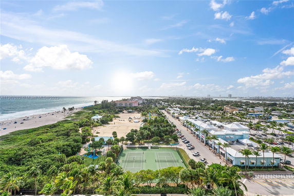 Aerial view of a coastal area with buildings, a tennis court, and a beach.