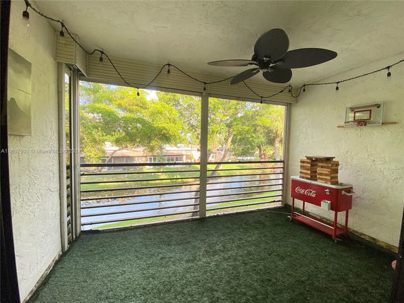 Covered outdoor area with artificial grass and ceiling fan, featuring a view of surrounding greenery and water.