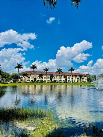 Distant view of a multi-story building with arches and palm trees near a body of water under a clear blue sky.