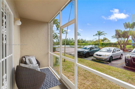 View from a patio overlooking a parking area with cars and greenery.