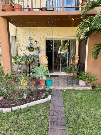 View of a patio area with potted plants and chairs in front of a house.