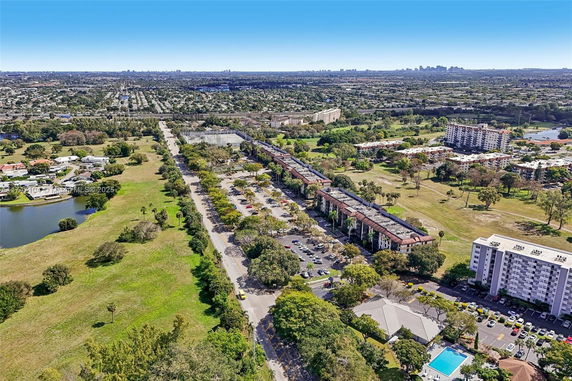 Aerial view of a residential area with apartment buildings and a swimming pool, surrounded by green spaces and roads.
