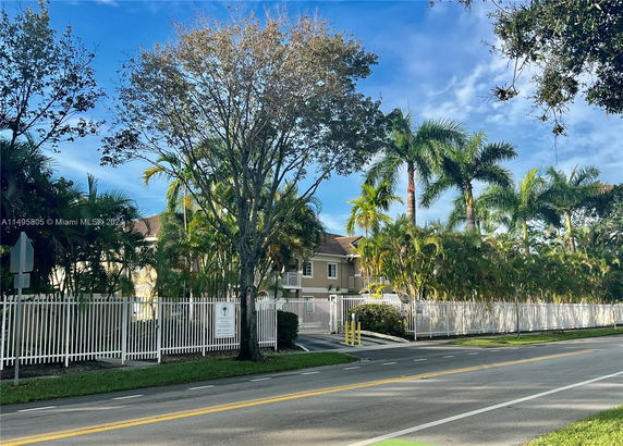 Front view of a two-story house with a fenced yard and palm trees.