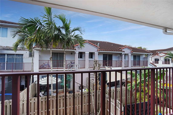 View from a balcony overlooking residential townhouses with palm trees.