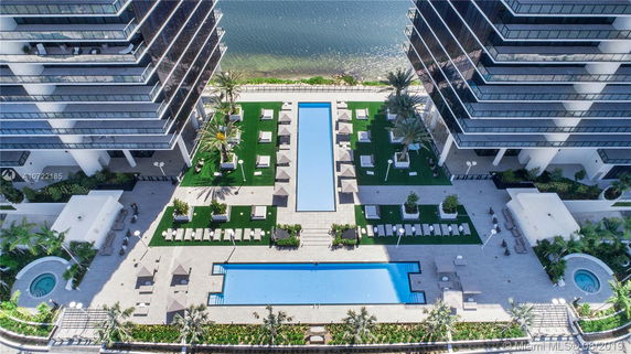 Aerial view of two modern high-rise buildings with glass facades, featuring a landscaped outdoor area with pools and seating.