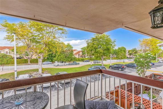 View from a balcony overlooking a parking lot and trees with residential buildings in the background.