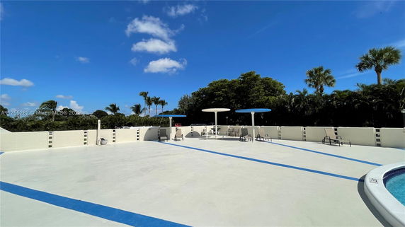 Rooftop area with lounge chairs and parasols, bordered by a low wall, surrounded by trees and blue sky.