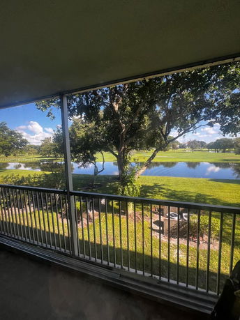 View of a grassy area with trees and a pond seen from a covered balcony.