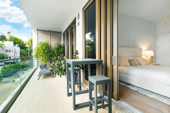Balcony view with potted plants and patio furniture, overlooking surrounding buildings and greenery.