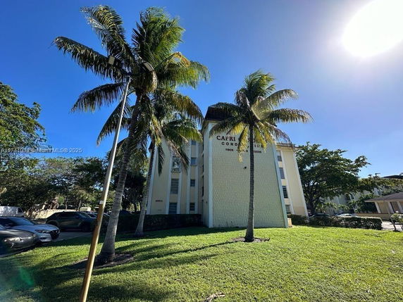 Front view of a multi-story condominium building with palm trees in front.
