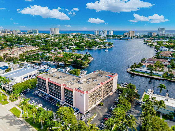 Aerial view showcasing a waterfront cityscape with a prominent multi-story building, waterways, and distant high-rise buildings.