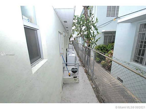 Narrow alleyway between two buildings with air conditioning units and a fence.