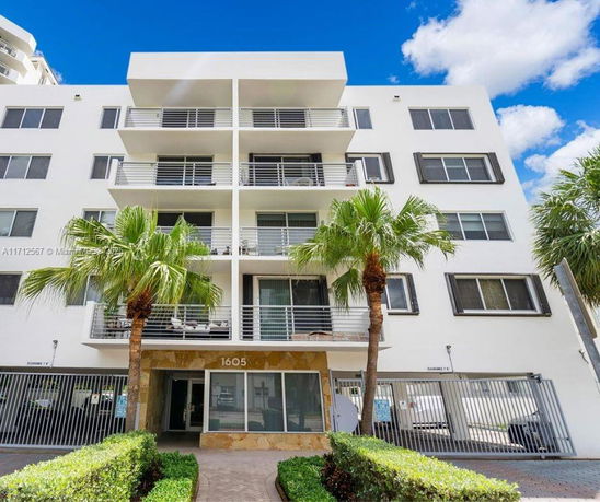 Front view of a multi-story residential building with balconies and palm trees.