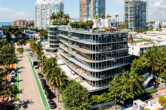 Front view of a modern multi-story glass building with balconies and rooftop greenery.