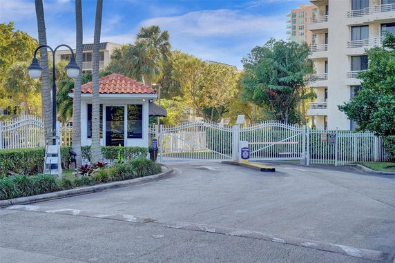 View of a gated entrance with a security booth in front of a multi-story building.