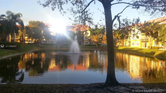 View of a building complex with reflections on a pond and a fountain in the foreground.