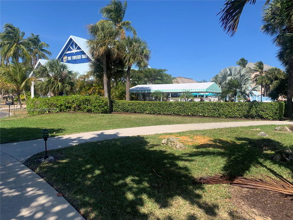 View of a structure with signage in a park-like setting with palm trees and pathways.