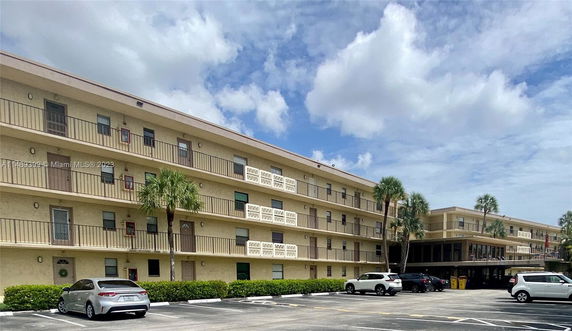 Front view of a multi-story apartment building with balconies and parking area.