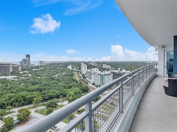 Panoramic view from a high-rise balcony overlooking a cityscape with buildings and greenery.