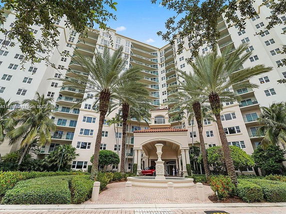 Front view of a multi-story residential building with palm trees and an entrance driveway.