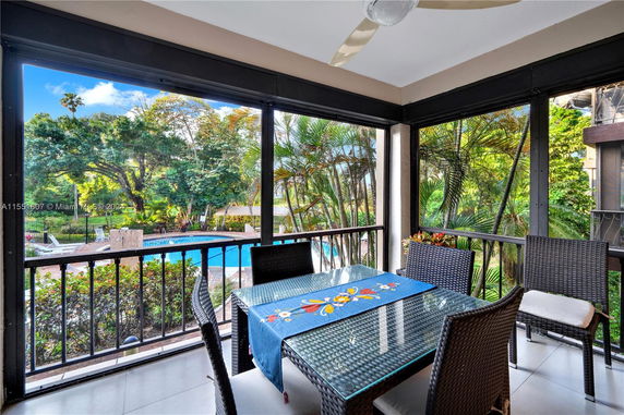 View from an outdoor seating area with table and chairs overlooking a swimming pool and lush greenery.