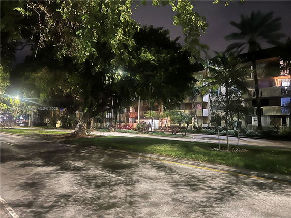 Nighttime view of a multi-story building with balconies and surrounding trees.