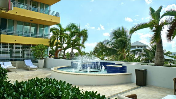 Outdoor area with a central round fountain next to a multi-story building and palm trees.