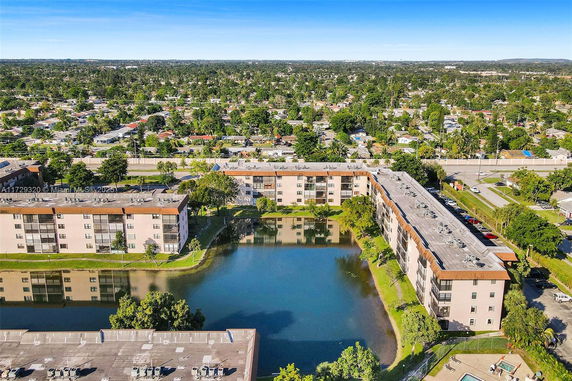 Aerial view of apartment complex with surrounding residential area and pond.