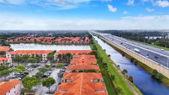 Aerial view of residential buildings with red roofs next to a highway and a water canal.