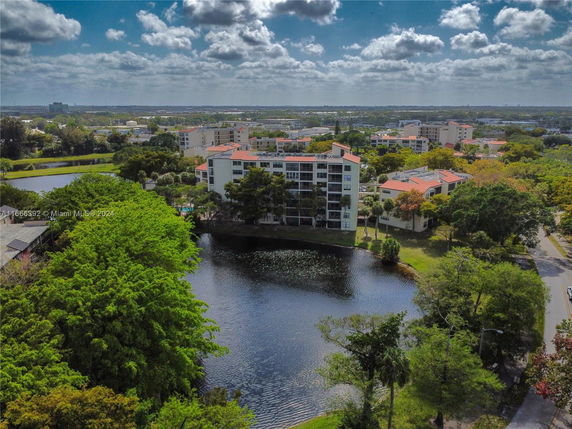Aerial view of an apartment building surrounded by trees and a body of water.