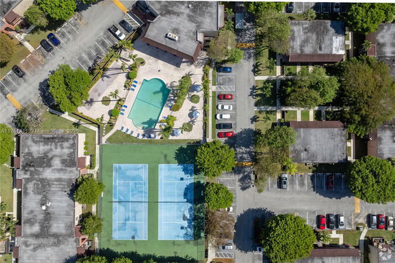 Aerial view of a residential area with a swimming pool, parking lot, and tennis courts.