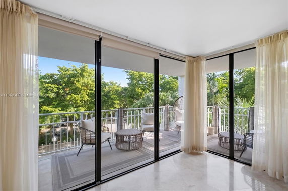 View of lush greenery seen from a balcony with glass railings and outdoor furniture.