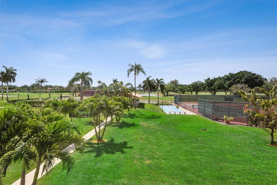 Outdoor view with palm trees, grass, and tennis courts in a park-like setting.